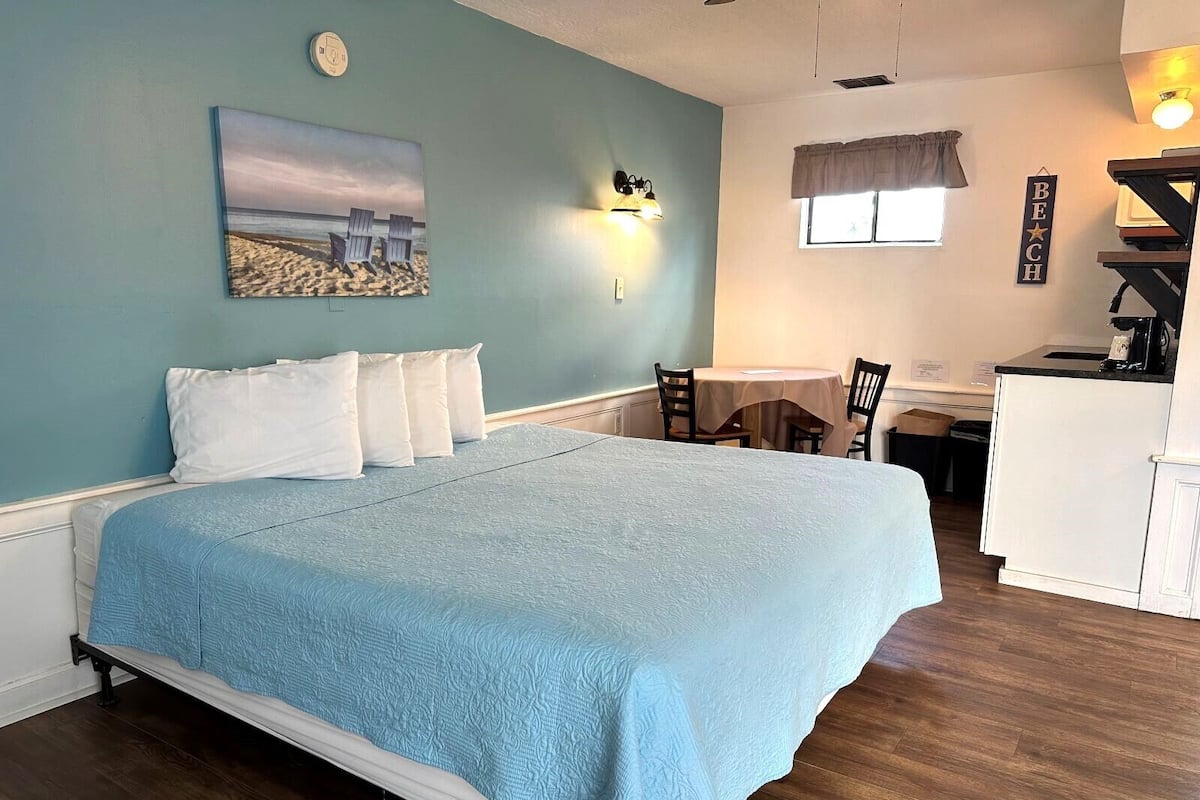 A bedroom with a bed, a desk, and a kitchenette.