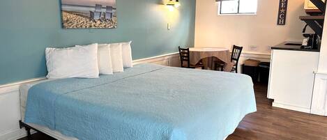 A bedroom with a bed, a desk, and a kitchenette.