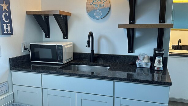 A compact kitchen with a microwave, sink, and a decorative sign above the sink. - Nautical Motel (Hampton)