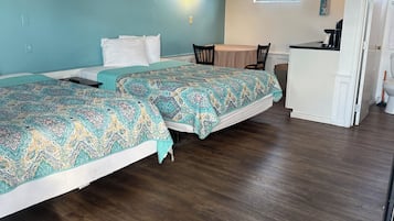 A room with two beds, a ceiling fan, a small kitchenette, and a window.