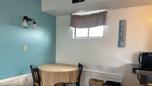 A small kitchenette with a table and chairs, a window with a curtain, and a sign on the wall. - Nautical Motel (Hampton)