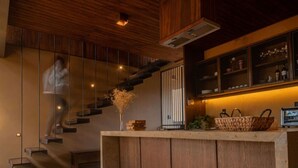 Een moderne keuken met houten kastjes, een vast eiland en een trap met glazen balustrade.