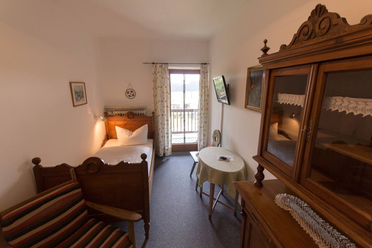 A bedroom with a bed, a chair, a table, a dresser, and a television.