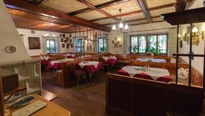 A traditional inn with wooden beams and a high ceiling, featuring multiple dining tables with red tablecloths and wooden benches. - Landhaus Griessee (Obing)