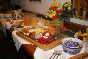 A buffet table with various food items, a fruit bowl, and a decorative vase with flowers. - Landhaus Griessee (Obing)