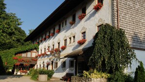 A traditional building with a stone facade, multiple windows, and red flower boxes. - Landhaus Griessee (Obing)