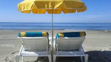 Relax in comfort on the beach with two lounge chairs and a shaded umbrella.