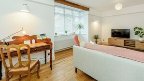Un salon moderne avec un bureau en bois, un canapé confortable, une télévision et une fenêtre équipée de stores.