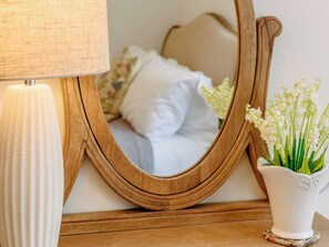 A wooden-framed mirror with a white lamp beside it, reflecting a bed and a vase with flowers. - 3 bedroom accommodation in Selsey (Selsey)