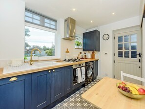 A modern kitchen with a built-in washing machine, a large window, and a dining area with a fruit bowl. - 3 bedroom accommodation in Selsey (Selsey)