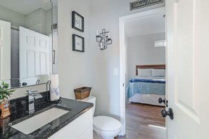 Un bany amb un lavabo, un vàter i un mirall. Es veu un llit per una porta oberta a l'habitació adjacent.