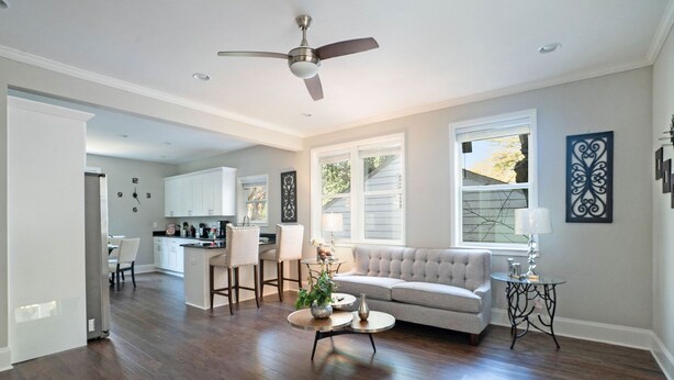 A spacious living room with a sofa, coffee table, and a ceiling fan. A kitchen is visible in the background with white cabinets and a dining area. - Mega Master Suite 4 miles to Mercedes Benz Stadium (4 Smart TVs) (Atlanta)