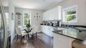 A modern kitchen with white cabinets, a granite countertop, and a dining area with a glass table and chairs. - Mega Master Suite 4 miles to Mercedes Benz Stadium (4 Smart TVs) (Atlanta)