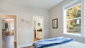 A bedroom with a bed, a window with a view of trees, and a hallway leading to a bathroom. - Mega Master Suite 4 miles to Mercedes Benz Stadium (4 Smart TVs) (Atlanta)