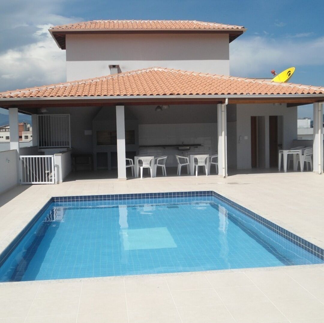 A swimming pool with a tiled deck, a covered patio area with chairs, and a satellite dish on the roof.