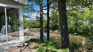 Eine Hängematte am Fenster mit Blick auf einen Fluss, umgeben von Bäumen und einem Gebäude.
