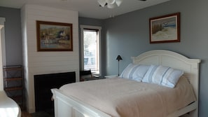 A bedroom with a bed, a fireplace, a window with blinds, and two framed pictures on the wall. - Spacious 4BR Beach Home. Private fenced Yard & Decks. Easy bike ride to town, (Rehoboth Beach)
