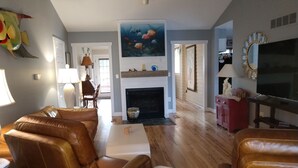 Ein Wohnzimmer mit Kamin, Ledersofas, einem Fernseher und einem großen Wandgemälde mit Fischen.