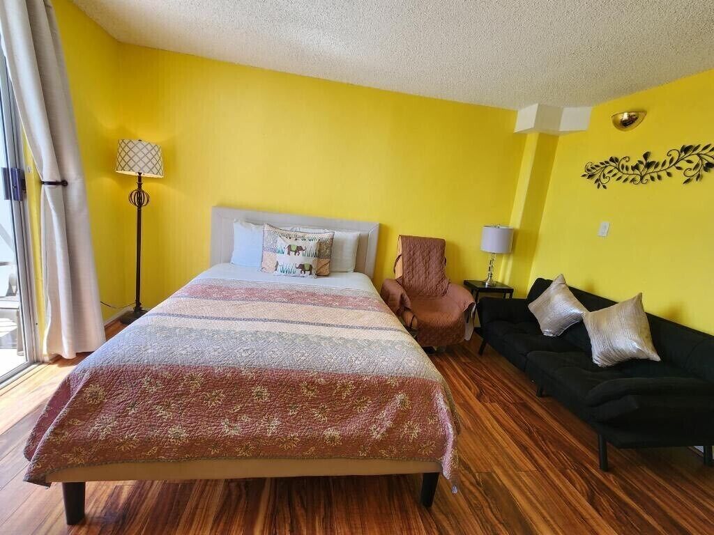 Una habitación con cama, sofá negro, lámpara y un adorno en la pared.