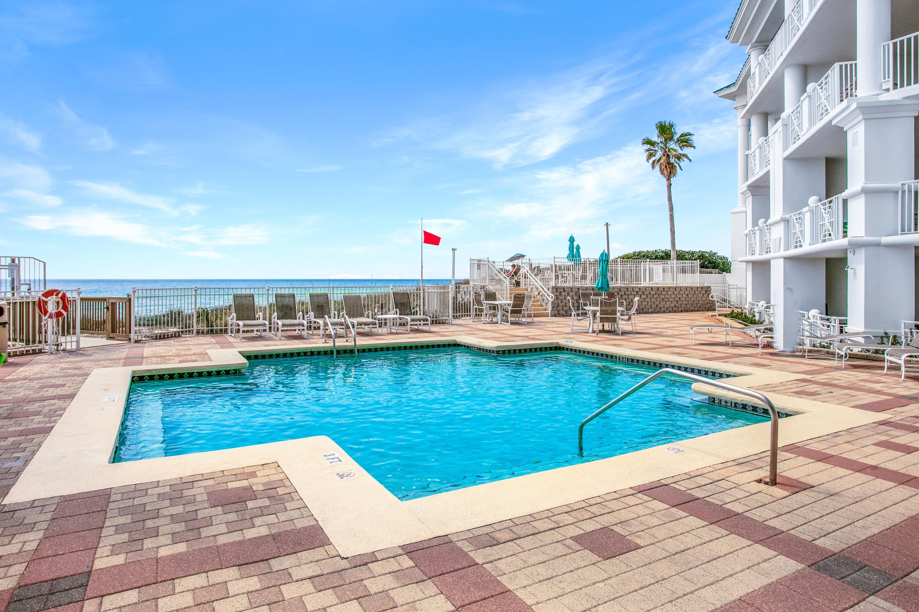 A pool area with a clear view of the ocean, a flag, and a palm tree.