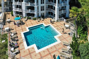 Une piscine sur le toit, dont le fond est décoré de motifs géométriques en mosaïque, entourée de chaises longues et de parasols.