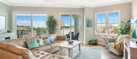 A spacious living room with a leather sofa, a wooden coffee table, and a view of a balcony with outdoor furniture.