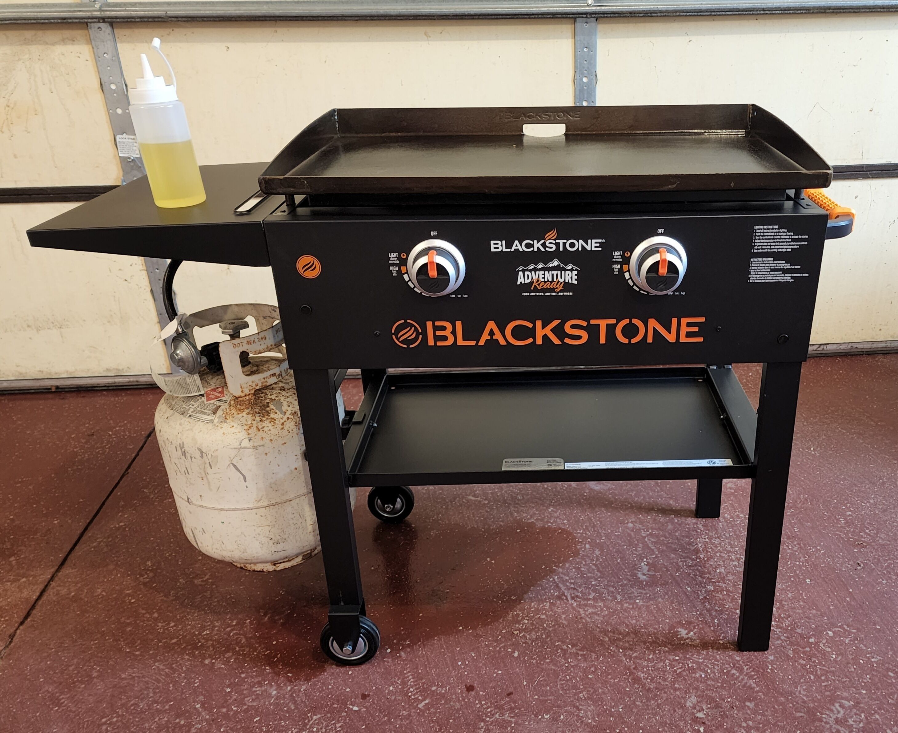 A portable Blackstone grill with two control knobs, a small shelf, and a gas canister.