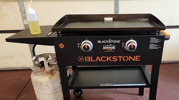 A portable Blackstone grill with two control knobs, a small shelf, and a gas canister.