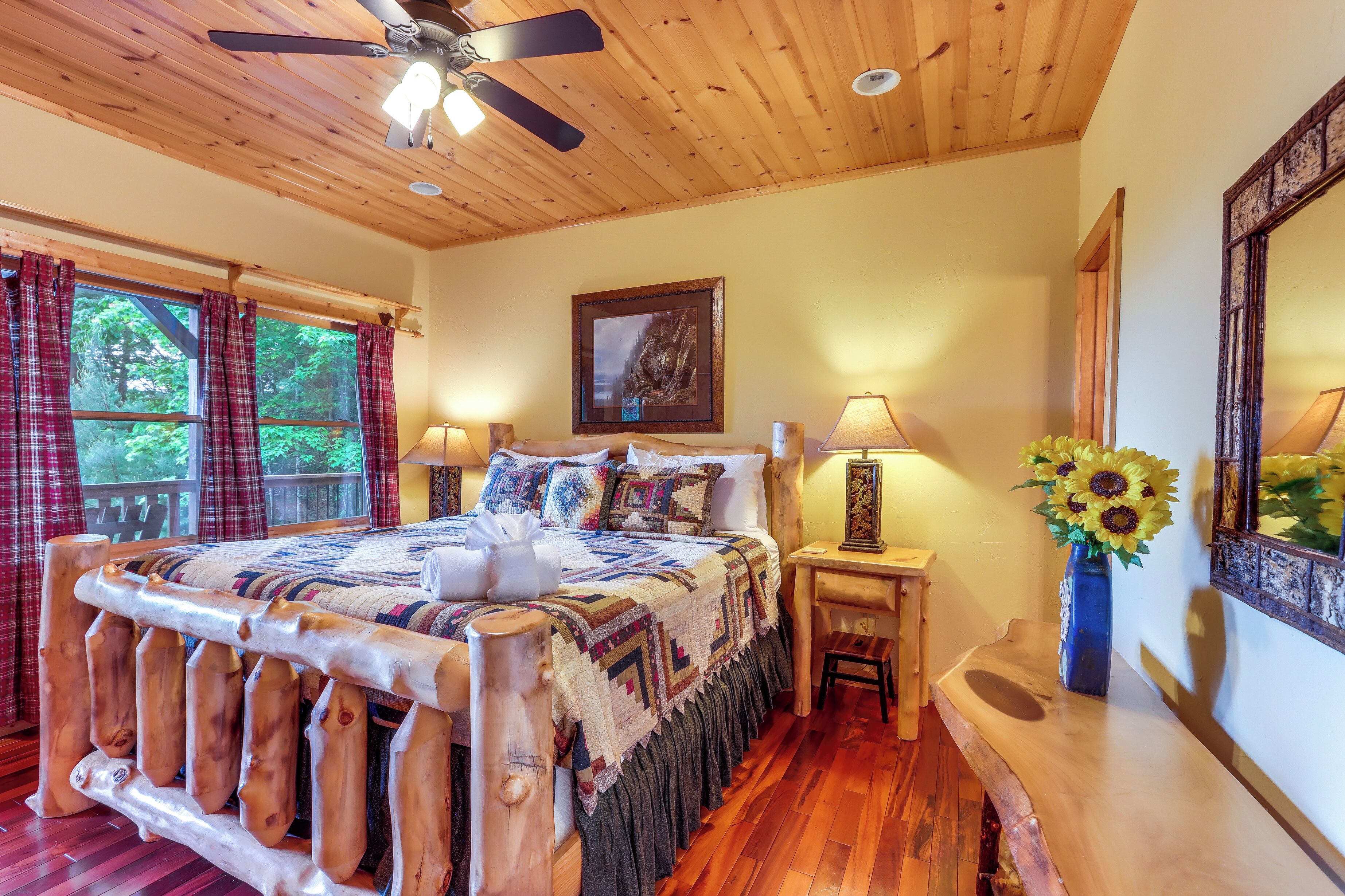 A wooden bed with a headboard, a nightstand with a lamp, a vase with sunflowers, and a painting on the wall.