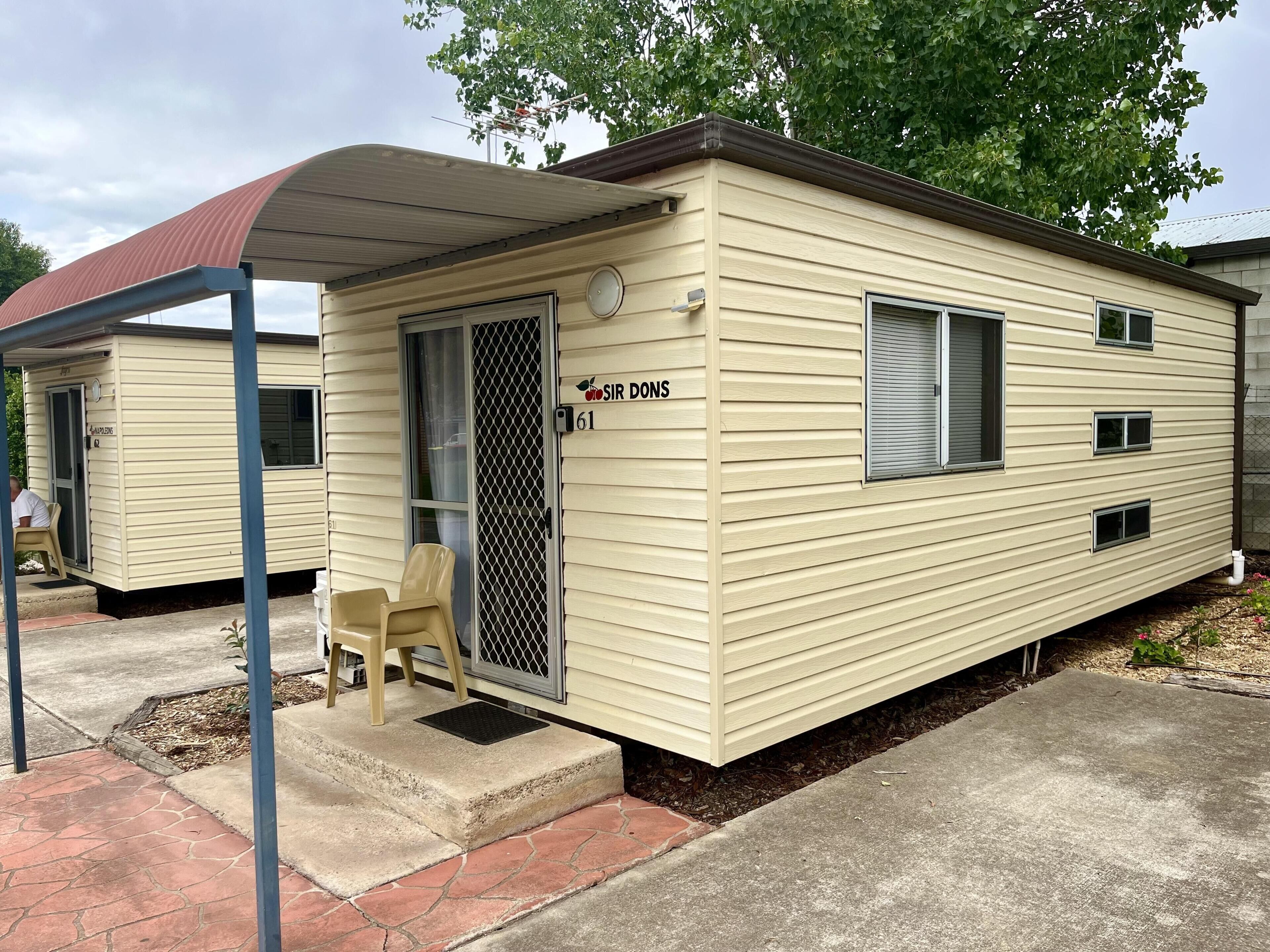 A mobile home with a covered porch, a door with a screen, and a small chair.
