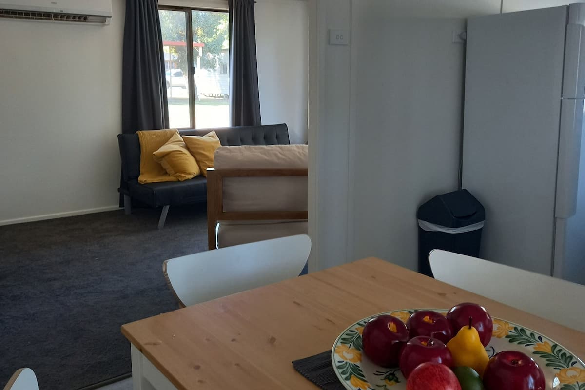 A dining area with a wooden table, a plate of fruit, and a sofa in the background.