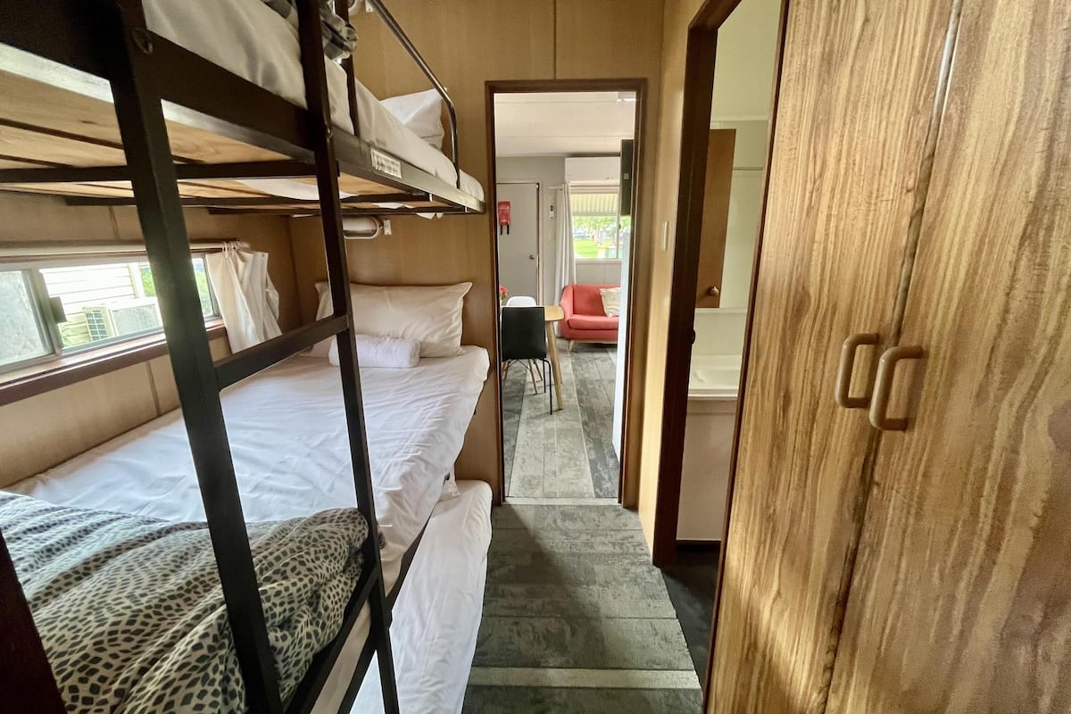 A bunk bed room with a wooden wardrobe, a red chair, and a view of the outside.