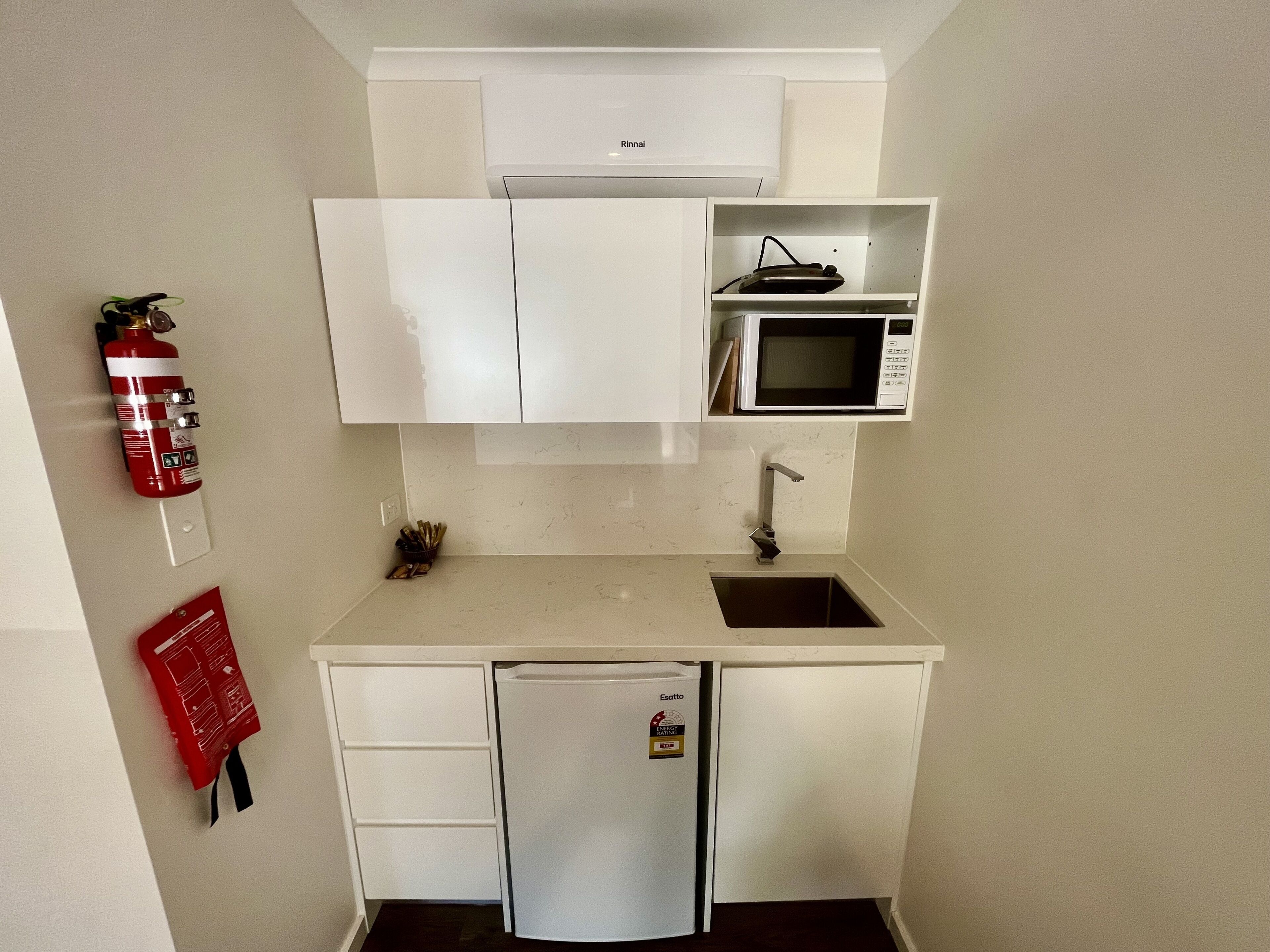Una kitchenette compacta con microondas, pileta y refrigerador.