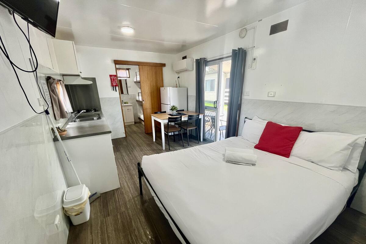 A hotel room with a bed, a desk, a chair, a television, and a kitchenette.