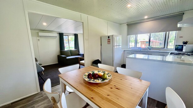 A modern kitchen with white cabinets, a wooden dining table, and a fruit bowl. - Young Tourist Park (Young)