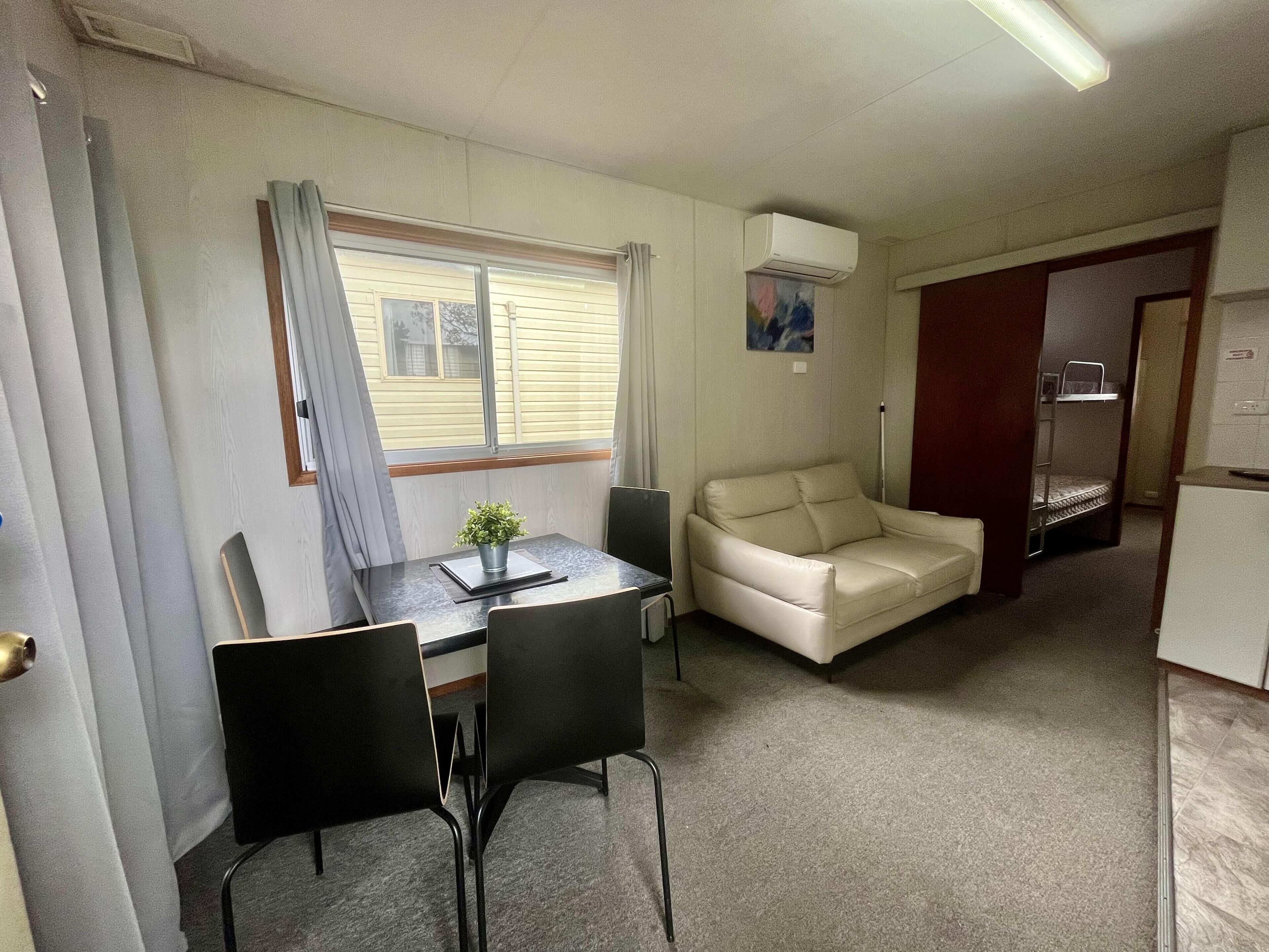 Una habitación compacta con mesa de comedor, sillas, sofá, litera y una pequeña cocina americana.