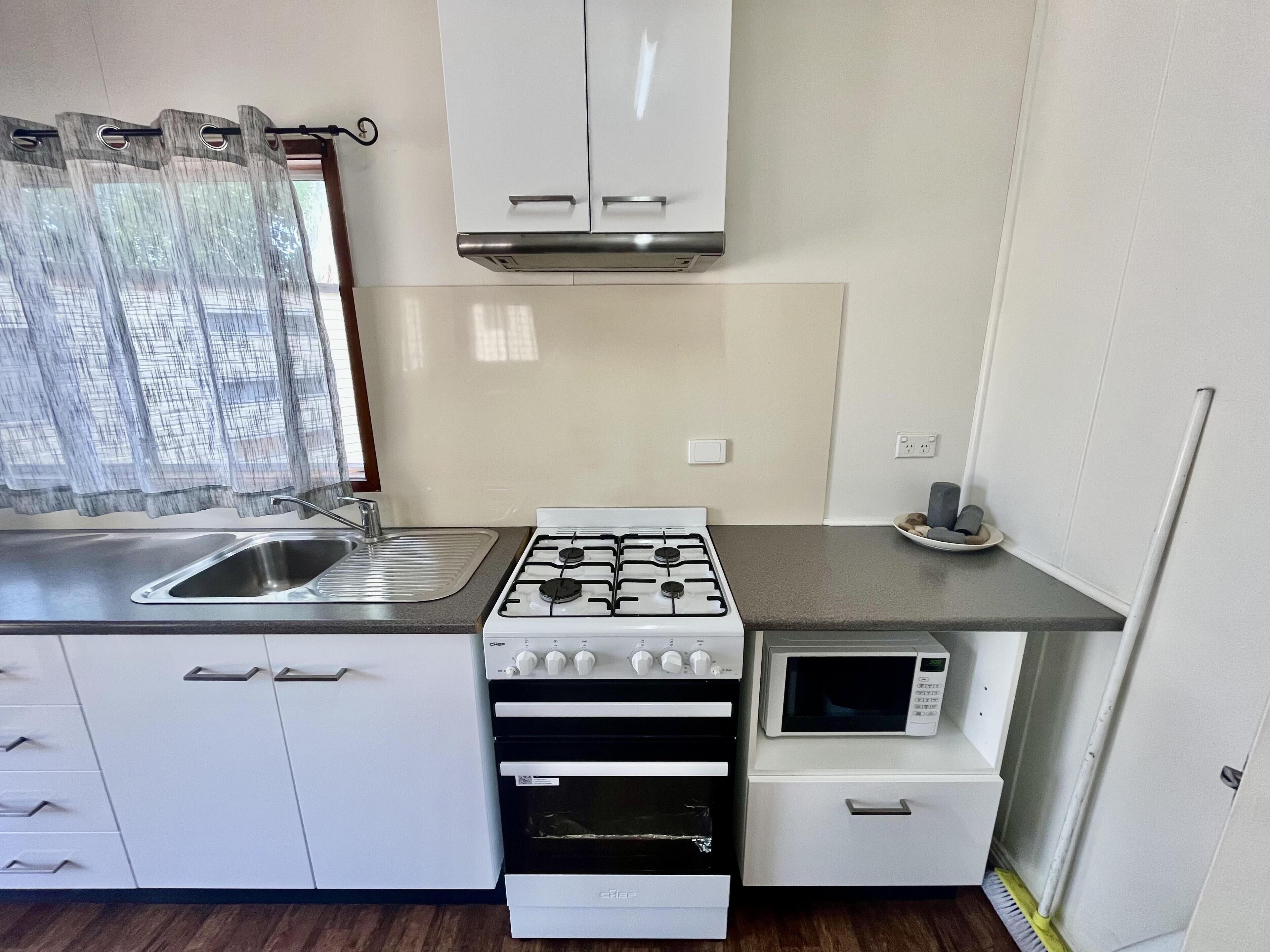 Uma cozinha compacta com fogão a gás, micro-ondas, pia e forno pequeno.