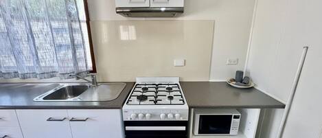 Uma cozinha compacta com fogão a gás, micro-ondas, pia e forno pequeno.