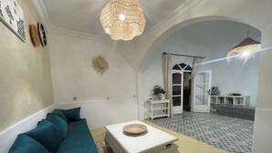 Een woonkamer met een blauwgroene bank, een witte salontafel, een geweven mand en een hanglamp.