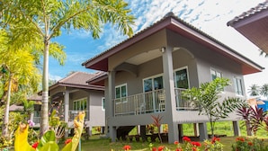 A two-story house with a balcony, surrounded by lush greenery and flowering plants. - Cozy cottage with kitchen of Maenam 4 (Koh Samui)