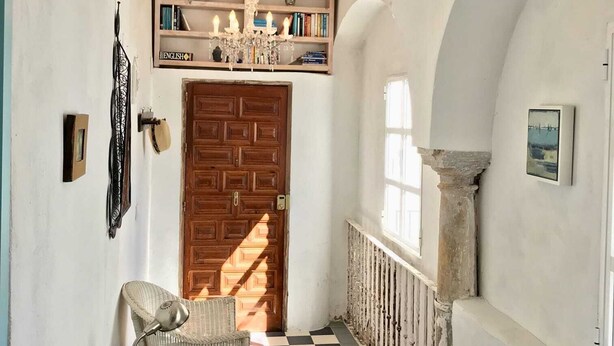 Un couloir orné d’un lustre, avec une porte en bois, des meubles en osier, un sol à carreaux et une bibliothèque.