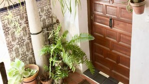 Une porte en bois ornée d’un panneau décoratif, une plante en pot et un luminaire suspendu.