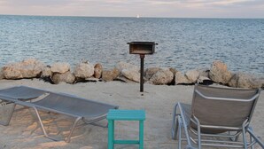 A beach with lounge chairs, a small table, and a metal grill.