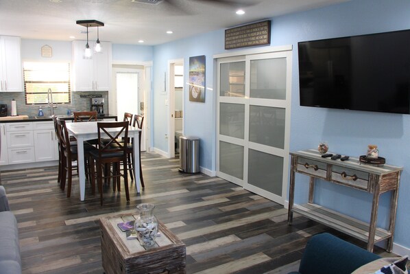 A modern kitchen with white cabinets, a dining area with wooden chairs, a TV mounted on the wall, and a console table with decorative items. - Waterfront Townhouse in Kawama (Key Largo)