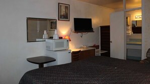 A hotel room with a bed, a desk, a microwave, a television, and a mirror. - Thunderbird Motel (Dodge City)