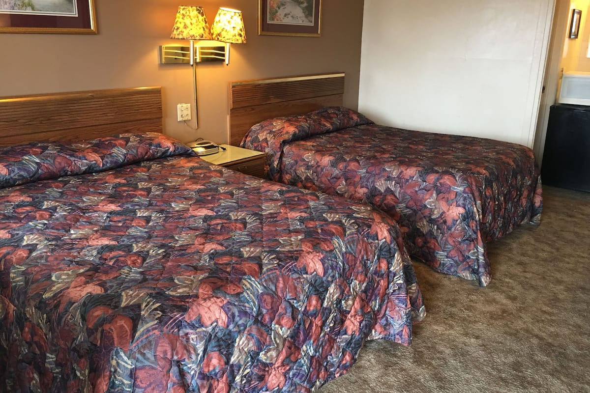 Habitación de hotel con dos camas, cada una con colcha estampada de flores, una mesita de noche, una lámpara y cuadros en la pared.