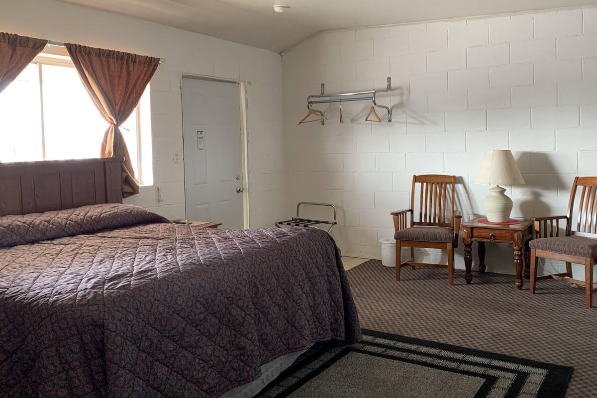 Habitación de hotel con una cama grande, dos sillones, una mesita de noche con una lámpara y un perchero.