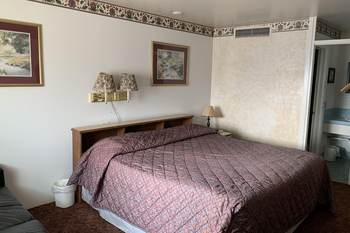 Un dormitorio con una cama grande, dos lámparas fijadas a la pared, un banco de madera y un cesto de basura pequeño.