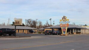 A motel with a sign indicating clean rooms, a drive-in window, and a parking lot with cars. - Thunderbird Motel (Dodge City)