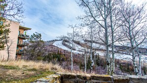 A stone retaining wall with a view of a hillside and a building with balconies. - Ski-In/Ski-Out Condo | Storm Meadows Club A! (Steamboat Springs)